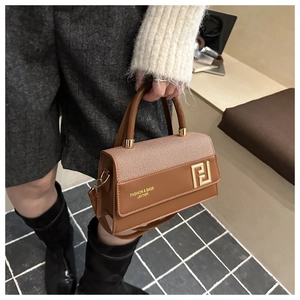 Detail of a brown leather handbag featuring woven texture and golden geometric hardware