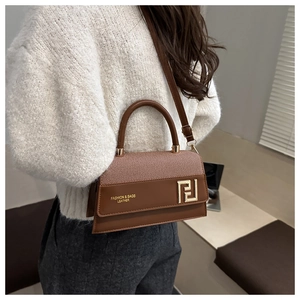 Detail view of a brown leather and twill crossbody bag with golden geometric clasp
