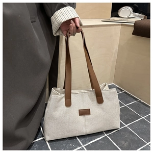Detailed close-up of beige canvas tote bag with brown leather handles and brand tag