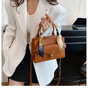 Detailed view of a brown leather crossbody bag with silk scarf handle and gold buckle