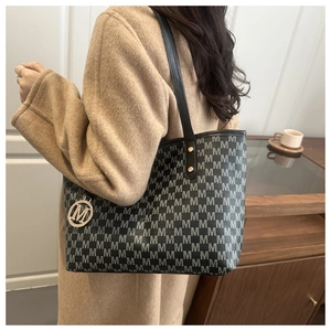 Détail du sac cabas monogramme gris avec rivets dorés et pendentif M sur manteau