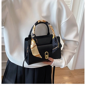 Detail of black PU leather handbag with gold oval twist lock and decorative handle scarf