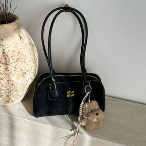 Elegante schwarze Wildleder-Tasche mit Goldlogo und Plüschbär-Anhänger für Winter 2025