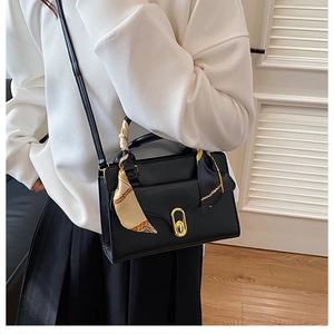 Close-up of a black crossbody bag with silk scarf handle and gold oval metal lock buckle