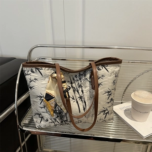 Canvas tote bag with black bamboo leaf print and brown handles in a lifestyle setting