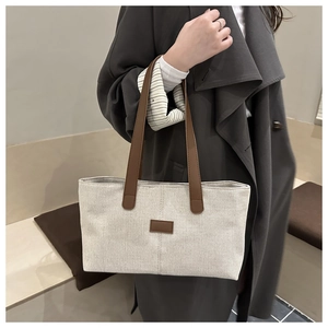 Detail of reinforced brown leather straps and small patch on cream canvas tote bag