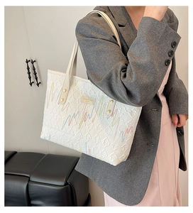 Detail of white quilted tote bag with colorful embroidery and gold metallic rivets
