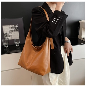 Caramel brown PU leather tote bag with wide shoulder strap shown in a modern cafe setting