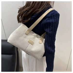 Detail of off-white canvas tote bag with brown leather handles worn by a model