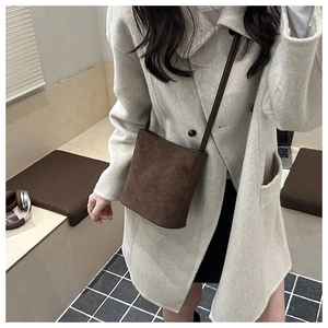 Detailed view of minimalist brown suede crossbody bag styled with a beige wool coat