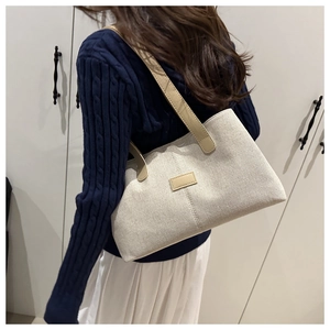Side view of large oatmeal canvas tote bag with brown leather handles on shoulder