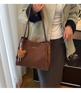 Detail of a brown matte leather shoulder bag with woven straps and a plush bear pendant