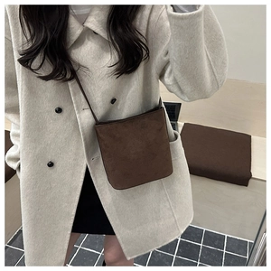 Macro shot of brown suede bucket bag texture on a model wearing a beige wool coat