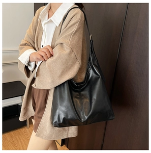 Detail of a large black faux leather tote bag with golden hardware and adjustable strap