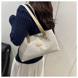 Detailed view of beige tote bag with brown leather straps worn on a person