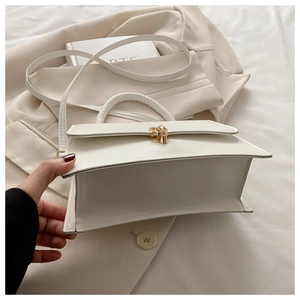 Detailansicht der Unterseite einer weißen Kunstledertasche mit goldenem Drehverschluss