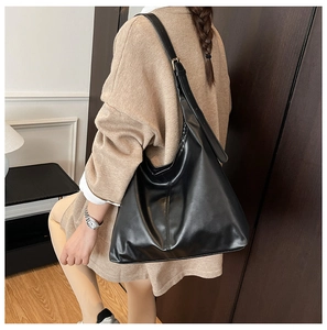 Model wearing a large black faux leather tote bag in a cozy indoor home setting