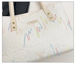 Detail of cream tote bag featuring 3D geometric embossing and colorful wavy embroidery