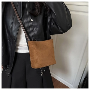 Detail shot of brown suede crossbody bucket bag styled with a black leather jacket