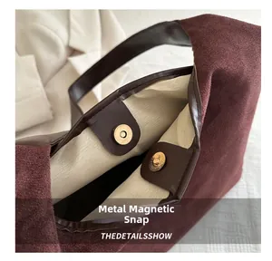 Detail of burgundy suede tote bag featuring dual golden magnetic snap closures and beige lining