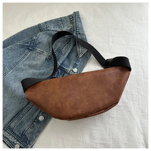Flat lay of a brown soft leather chest bag with black strap on denim jacket background