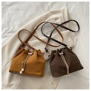 Close-up of suede drawstring bucket bags with gold chains and pearl pendants on fabric