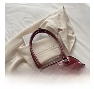 Detail of burgundy glossy leather handbag with bow decoration on stylish suit background