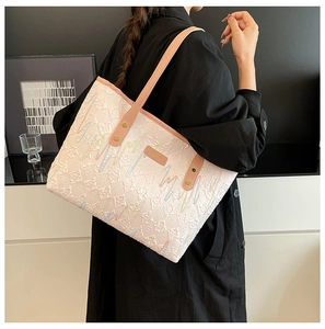 Detail of light-colored tote bag featuring 3D floral embroidery and leather handles