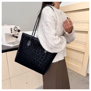 Detail view of large leopard print tote bag with black leather straps on a white sweater