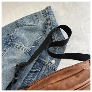 Close-up of a vintage brown PU leather sling bag lying on a denim jacket with strap detail