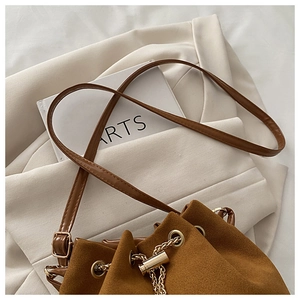 Detail of a brown suede bucket bag with gold chain drawstring and slim leather strap
