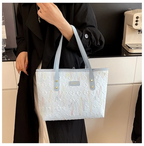 Close-up of light blue leather tote with letter E embossing and colorful wave embroidery