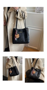 Detail of black tote bag featuring textured leather, woven straps and a plush bear charm