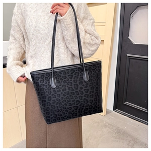 Detailed view of large black leopard print tote bag with long strap on a female model