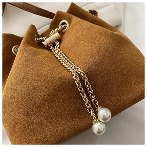 Close-up of matte brown bucket bag with gold chain and white pearl charms detail