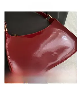 Detail shot of glossy burgundy patent leather half-moon bag with smooth gold hardware