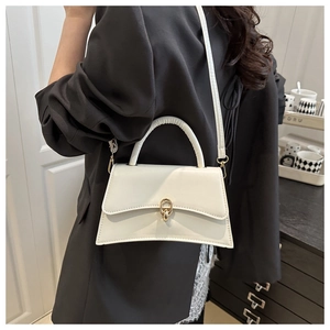 Weiße Trapez-Handtasche aus Kunstleder mit goldener Schließe an der Schulter eines Models