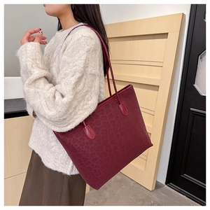 Detail view of burgundy tote bag with embossed leopard texture worn by a model