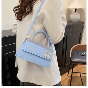 Détail du sac à main en cuir bleu clair avec logo doré et bordure pailletée sur mannequin