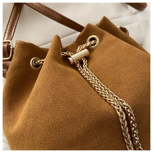 Detailed close-up of dark brown suede bucket bag with gold chain and metal eyelets