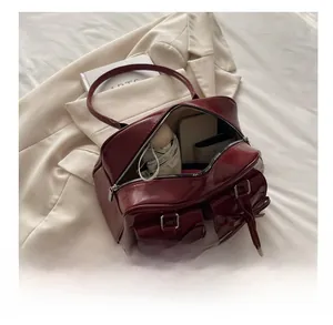 Detail showing the spacious interior of a burgundy patent leather bowling bag with daily items