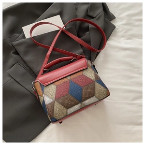 Detail view of a color-block square crossbody bag with red handle on grey blazer