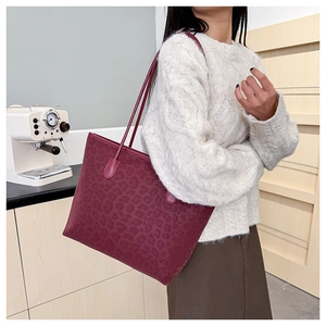 Close-up of wine red leopard print tote bag worn on shoulder by a model in soft lighting