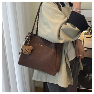 Detail of dark brown tote bag featuring braided handle and cute plush bear charm