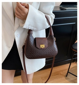 Détail du sac tressé en cuir marron avec boucle dorée sur une tenue blazer blanc