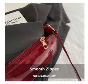 Detail of smooth golden metal zipper on a premium burgundy patent leather bag