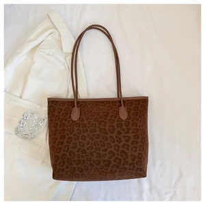 Detail view of large leopard print tote bag with brown straps on white fabric background