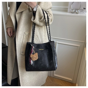 Detail of black tote bag with woven straps, gold logo, and a cute brown plush bear charm