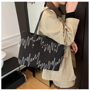 Detail of black tote bag with white wave texture and gold logo on leather shoulder strap