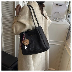Detail of black leather tote bag with woven handles and cute plush bear charm